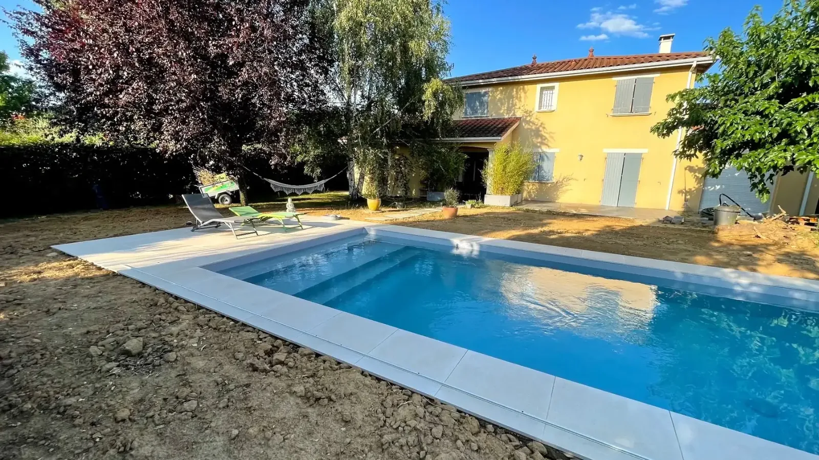 Piscine rectangulaire avec margelles claires réalisée par ST Création Paysage dans un jardin de l'Ain