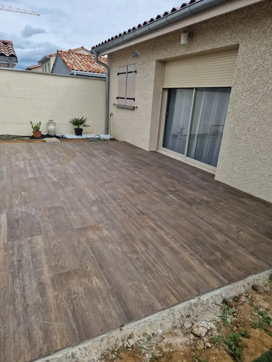 Terrasse en carrelage imitation bois posée contre une maison, réalisée par ST Création Paysage