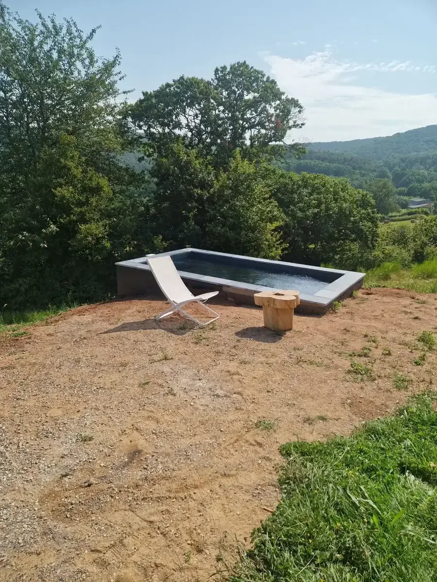 Bassin en béton avec margelles grises installé sur un terrain en hauteur dans l'Ain